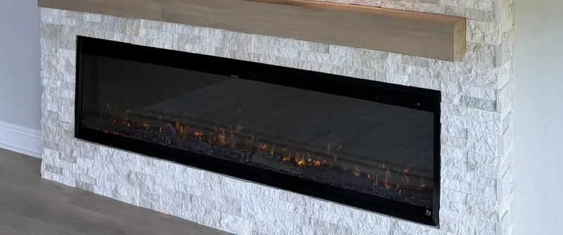 One long line of fire set into white stacked stone, under a light wood-tone mantel