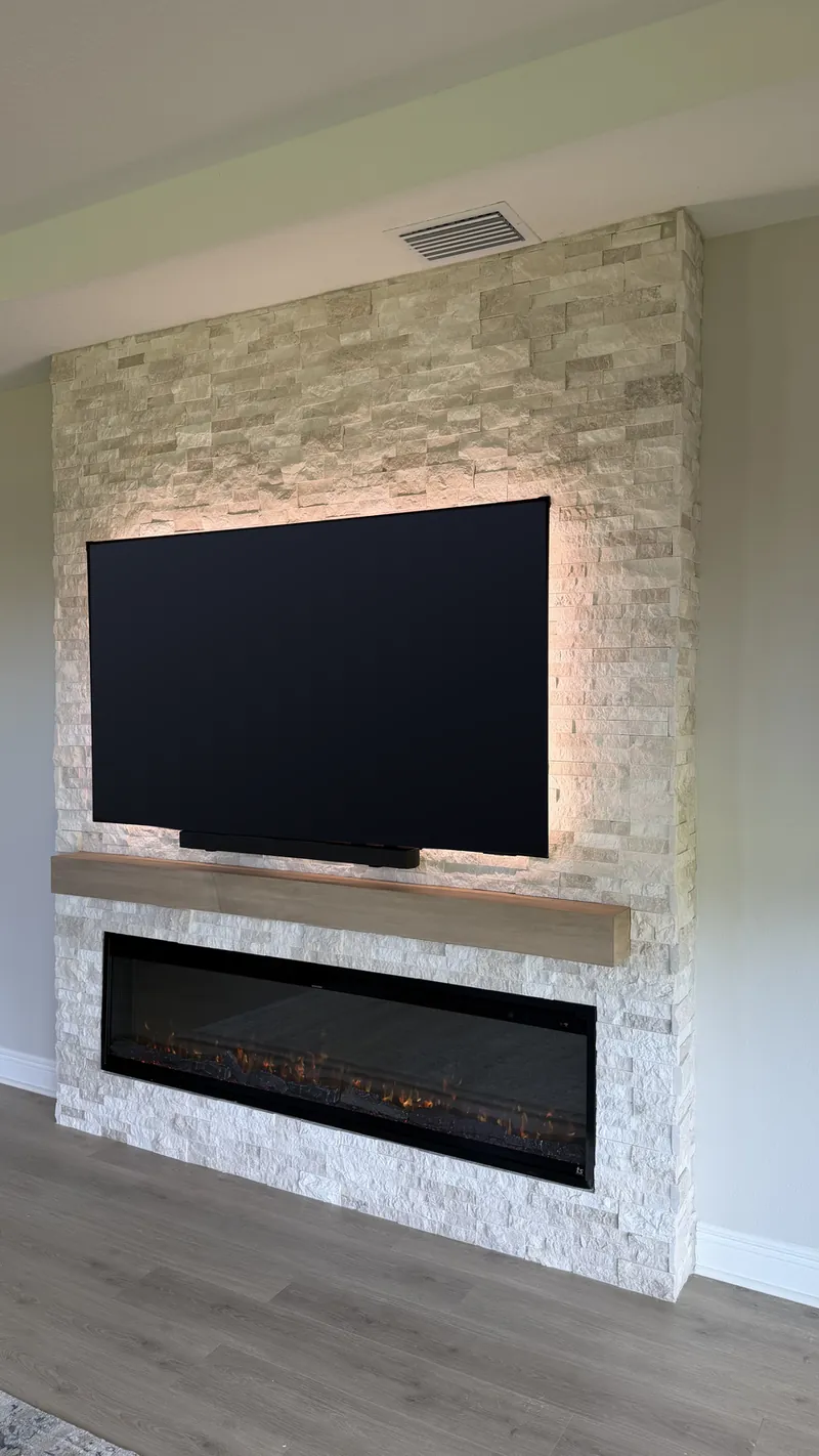 Stacked stone column with a warm glow behind the TV and a light wood-tone beam
