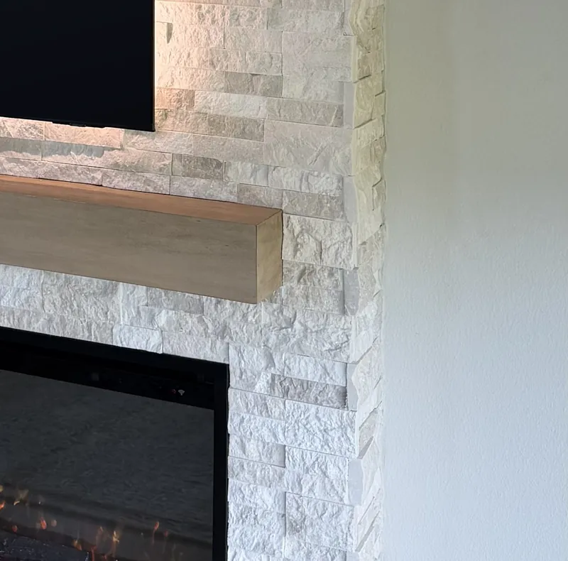 The end of the light wood-tone mantel and the stone turning the corner