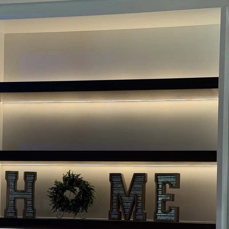 Lit dark shelves in a tall niche, with HOME letters and a wreath set on a shelf