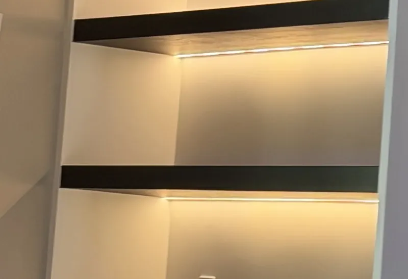 Two dark floating shelves in a white niche, each washed in warm light from below