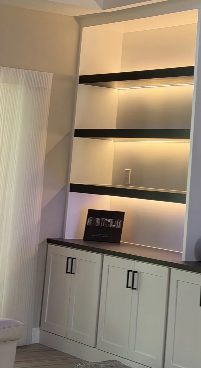 The left niche with warm lit dark shelves over white Shaker cabinets
