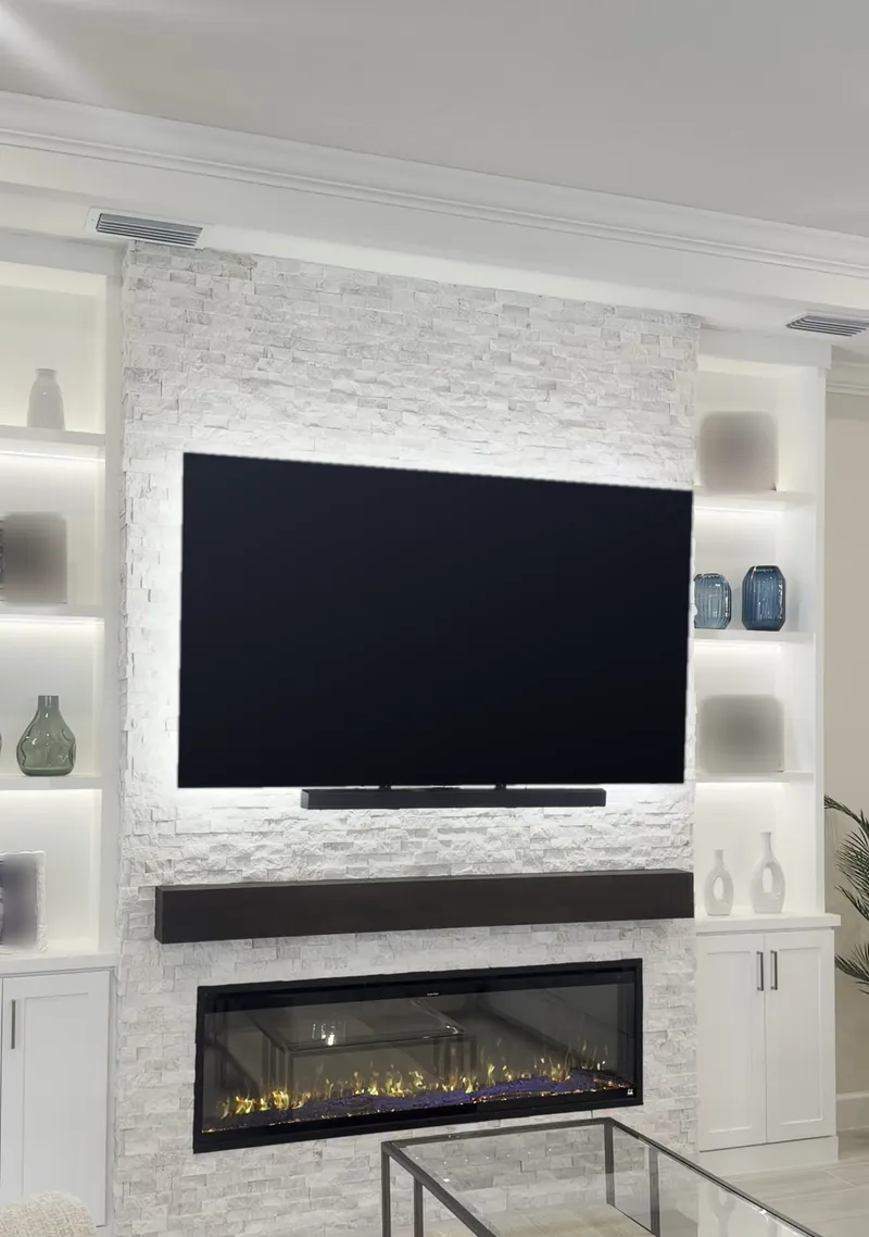 White stacked stone fireplace wall with a TV and soundbar, an espresso-tone mantel and a linear fireplace between two lit white towers over closed cabinets