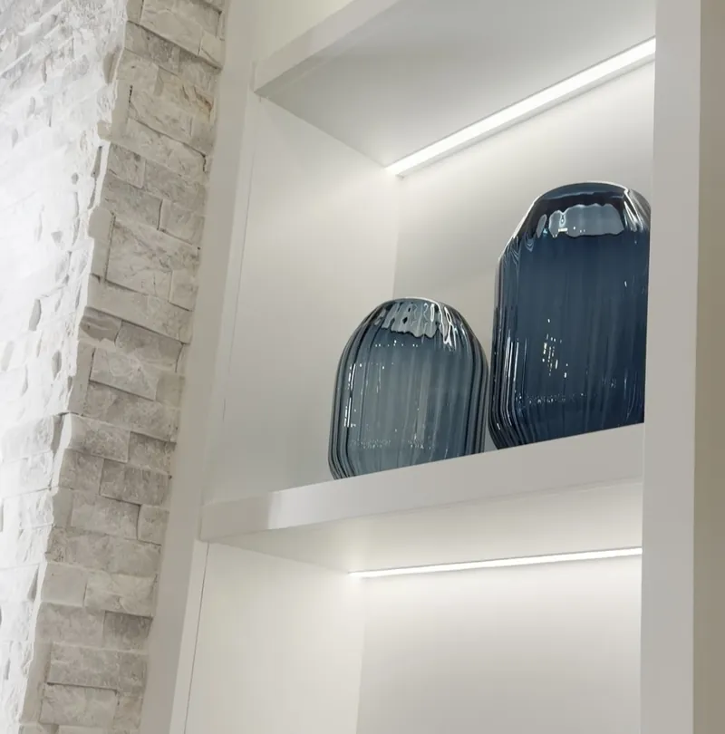 Close view of a lit tower shelf with blue glass vases, beside the stone