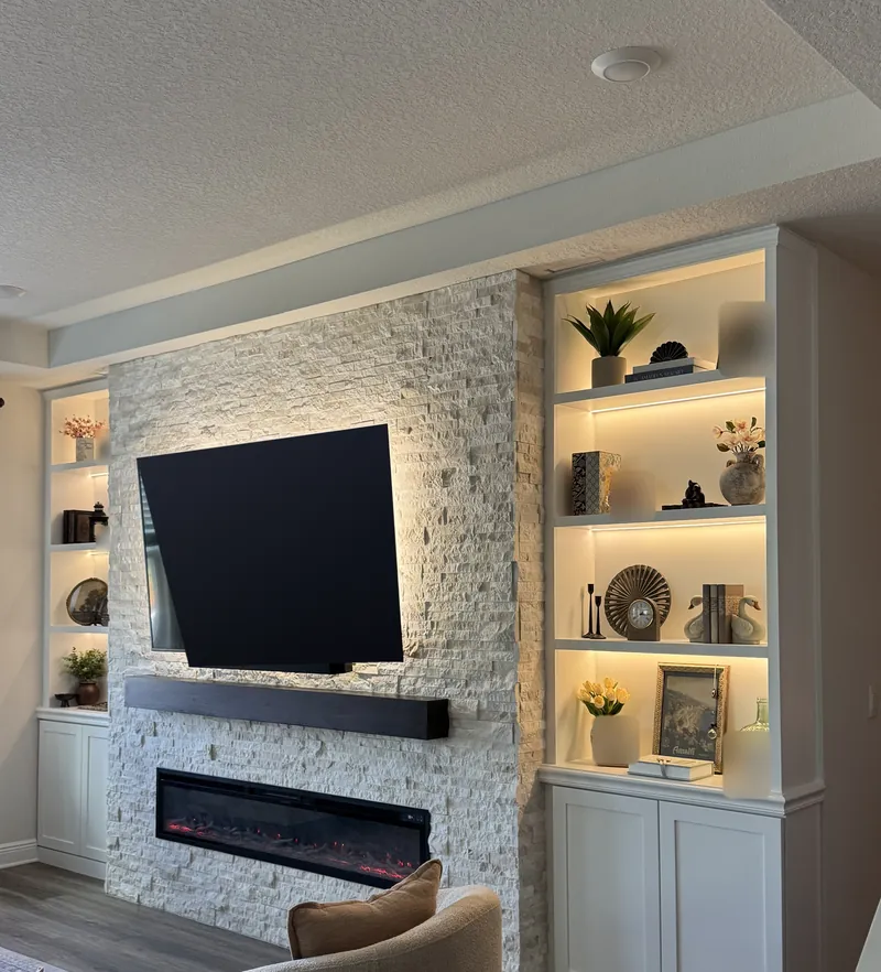 Stacked stone with a TV and a dark wood-tone mantel beside white built-ins with warm lit shelves