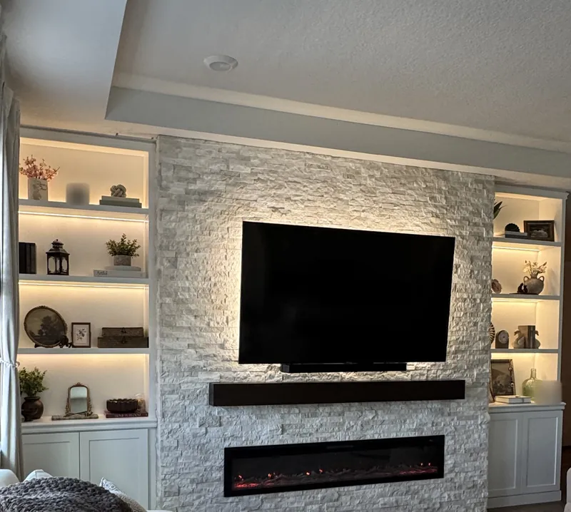 Cream stacked stone fireplace wall with a TV, an espresso-tone mantel, a linear fireplace and lit shelves on each side