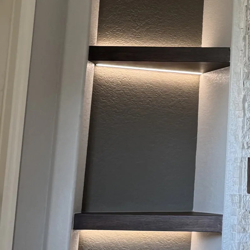 Two dark floating shelves lit from underneath in an arched niche