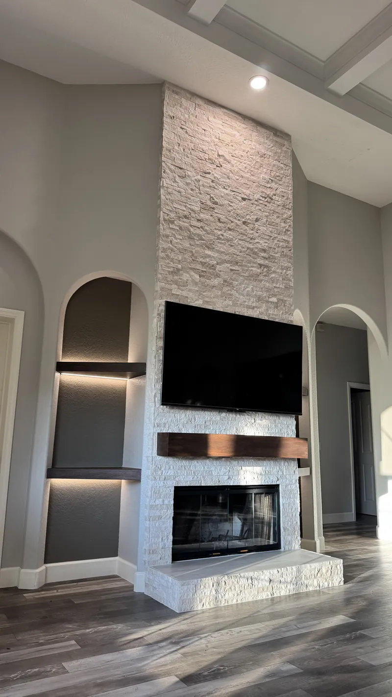 Lit dark shelves in an arched niche beside a stone fireplace wall with a dark mantel
