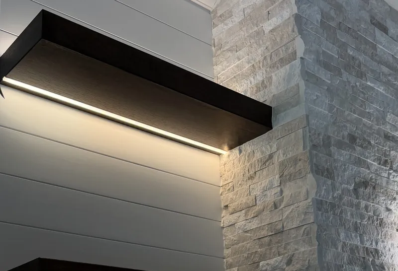 A dark floating shelf lit from below on white shiplap