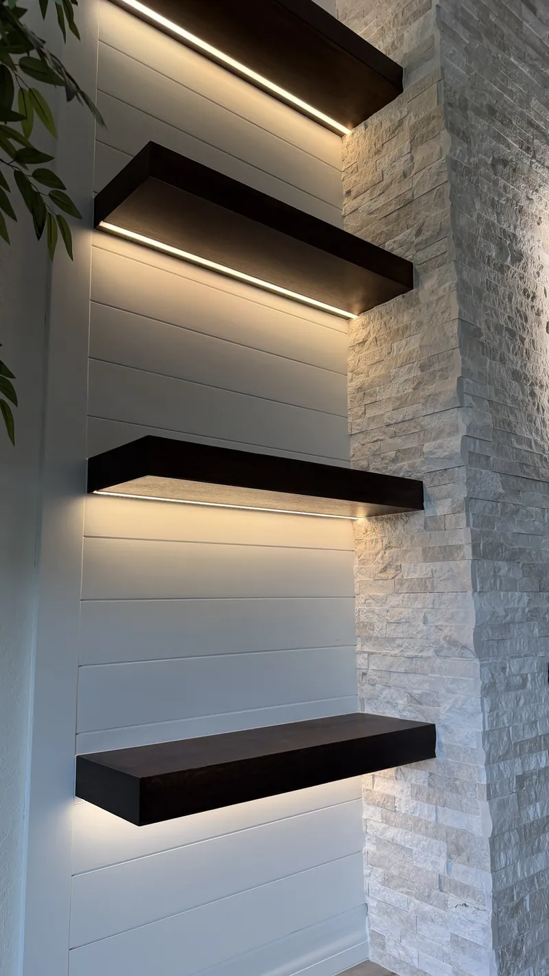 Espresso-tone floating shelves lit from below beside white stacked stone