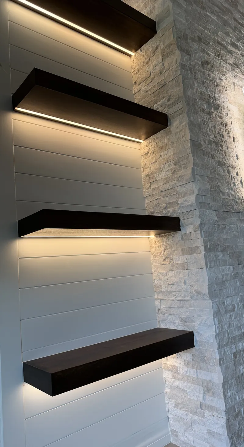 Espresso floating shelves lit from underneath on white shiplap, beside white stacked stone