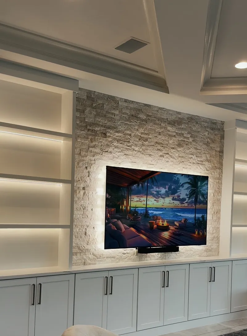 White media wall with stacked stone around the TV, lit shelves in white towers and cabinets below