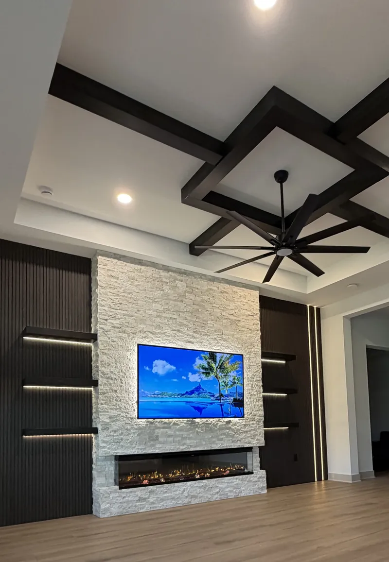 Fireplace wall in white stacked stone between dark fluted panels, with a three-sided fireplace under a dark beam ceiling