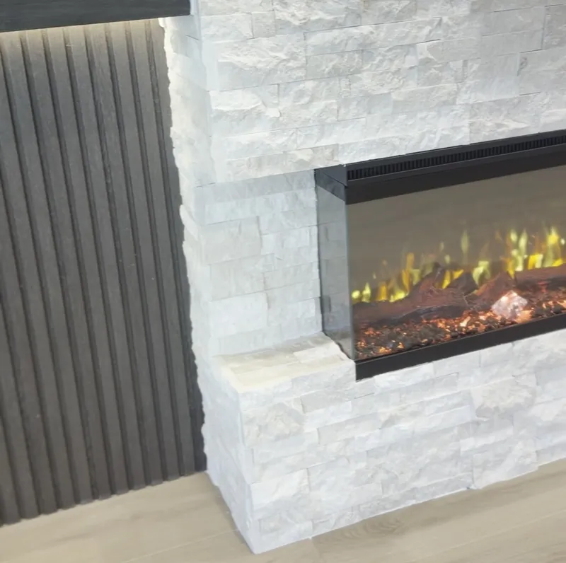 A three-sided linear electric fireplace set into white stacked stone, its glass wrapping the end