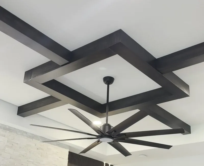 Dark wood beams crossing a white ceiling in a square pattern, around a ceiling fan