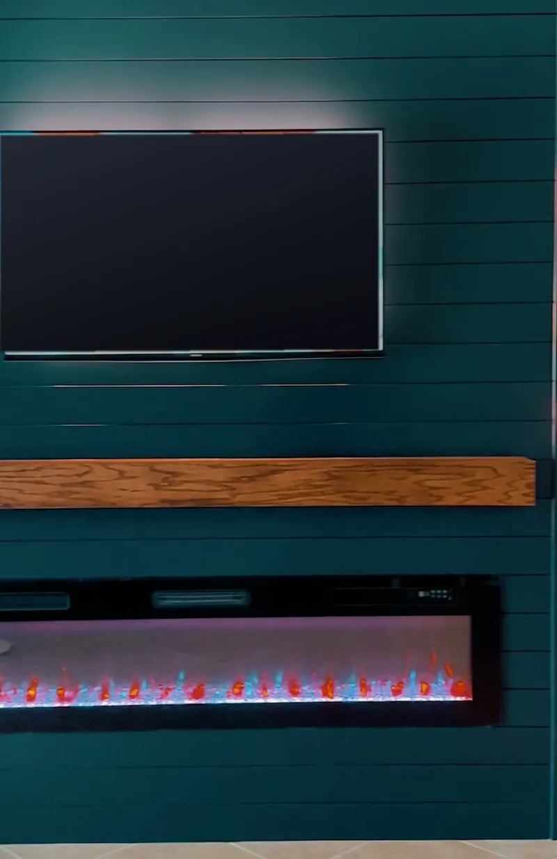Deep teal shiplap wall with a TV above a wood-tone mantel beam and a linear fireplace