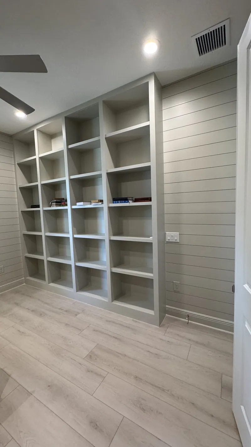 Floor-to-ceiling white open library shelving beside a shiplap wall